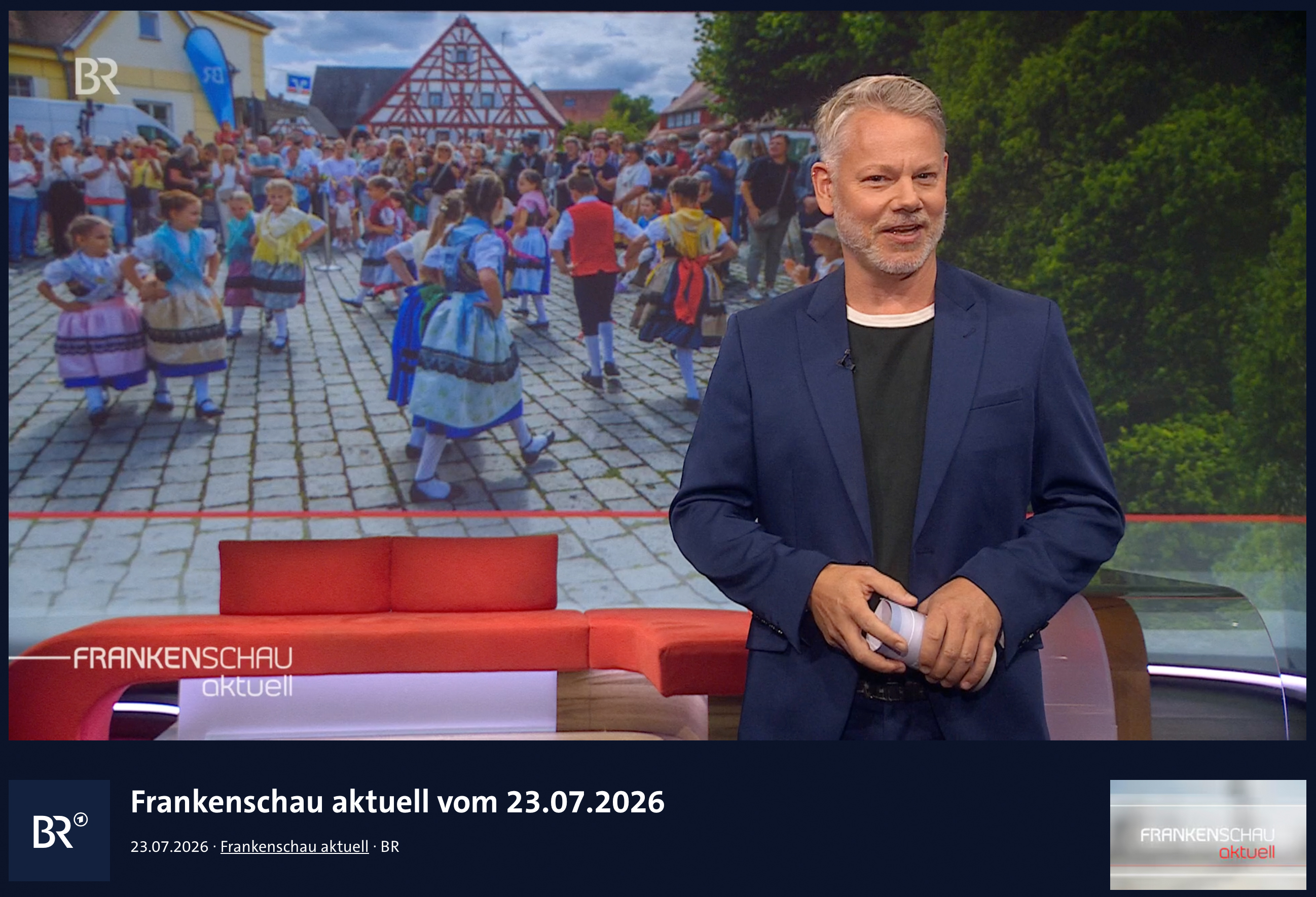 Frankenschau-aktuell-Moderator vor einem Foto der Kirchweih in Effeltrich