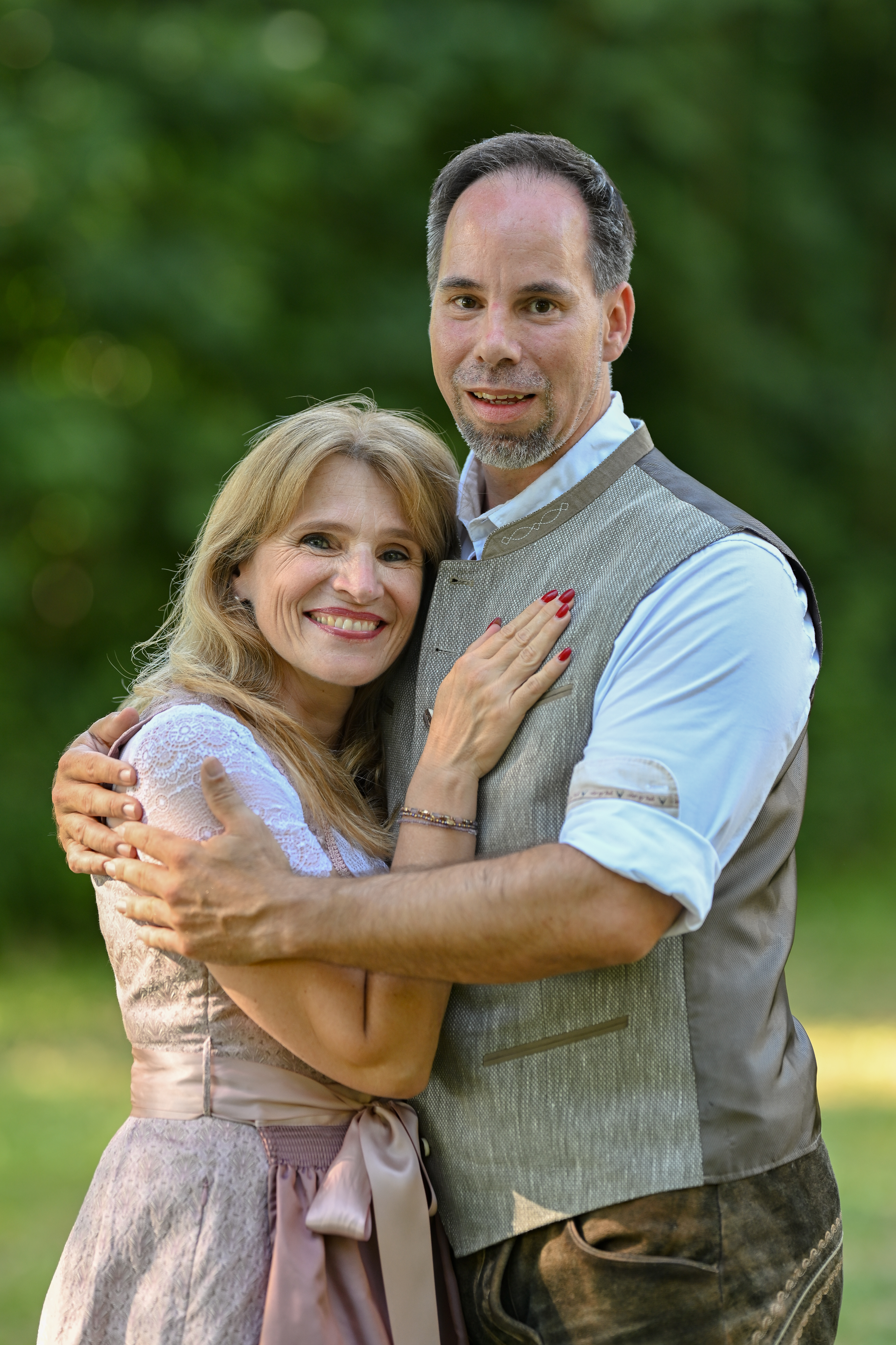 Petra und Markus umarmen sich vor grünem Hintergrund