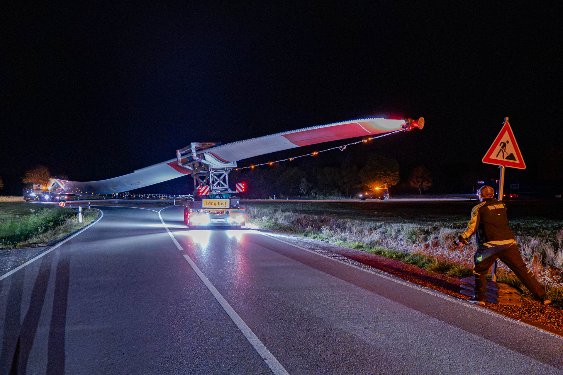 Rotorblatt auf einem Schwertransporter beim nächtlichen Rangieren, rechts ein Transportbegleiter