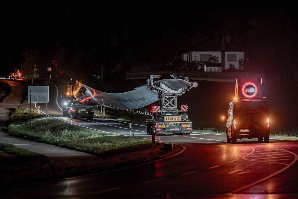 Langer Rotorblatttransport mit Begleitfahrzeug auf einer ansteigenden Straße bei Nacht
