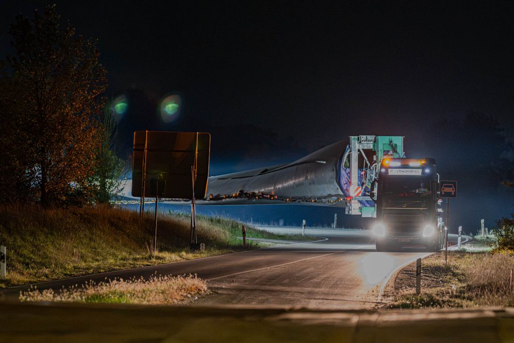 Zugmaschine kommt mit leuchtenden Scheinwerfern und einem Rotorblatt auf einer kurvigen Straße entgegen