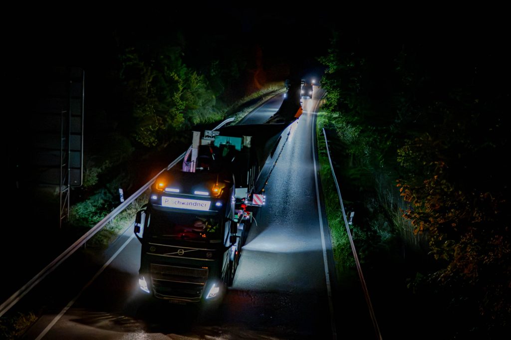 Schwertransporter mit Rotorblatt auf einer schmalen Straße bei Nacht, von oben gesehen