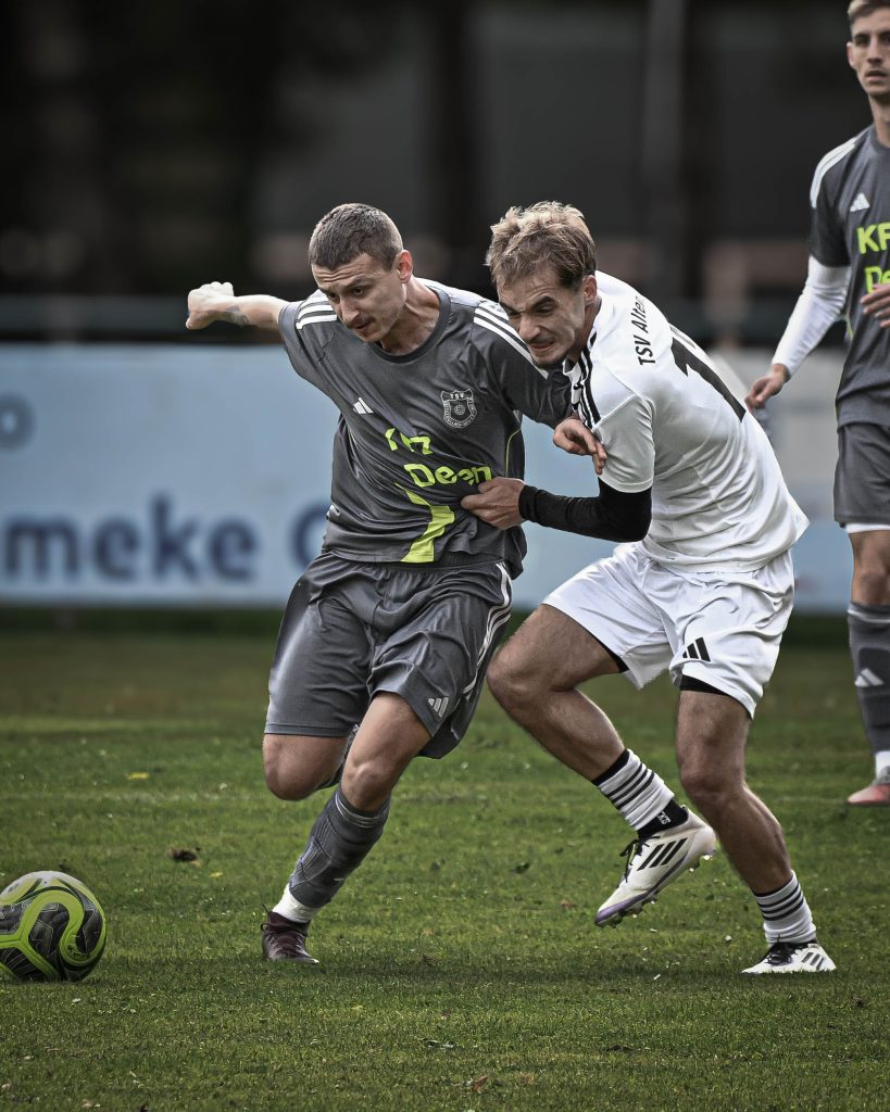 Fußballspieler in Grau und Weiß laufen eng nebeneinander zum Ball